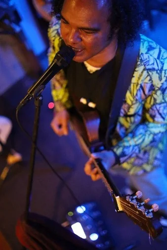 Dino Miranda singing and playing guitar in a patterned jacket