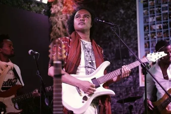 Dino Miranda playing a white electric guitar on stage